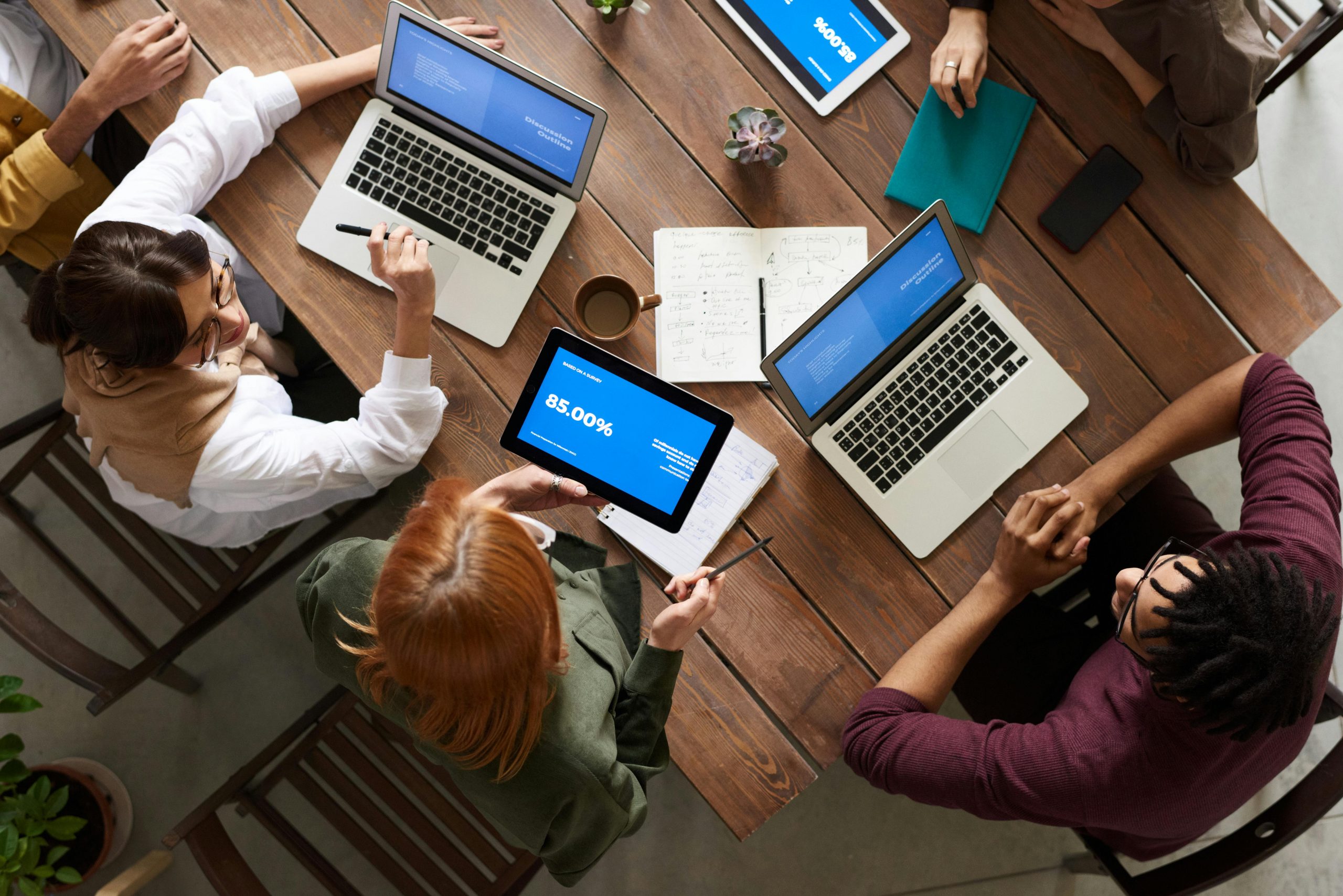 A group of people sit at a table with laptops, working together.