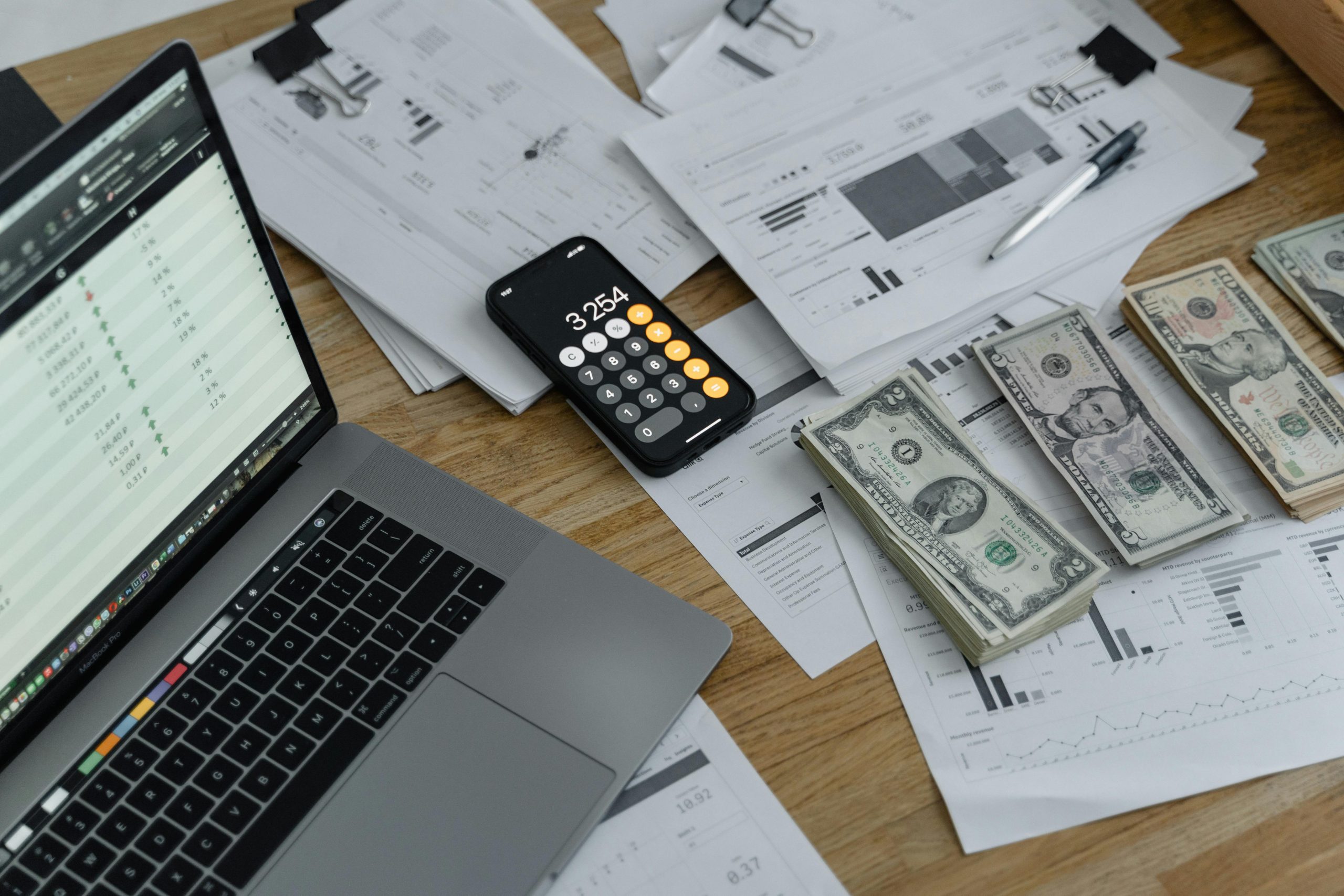 A computer, calculator, and money sitting on a tabletop.