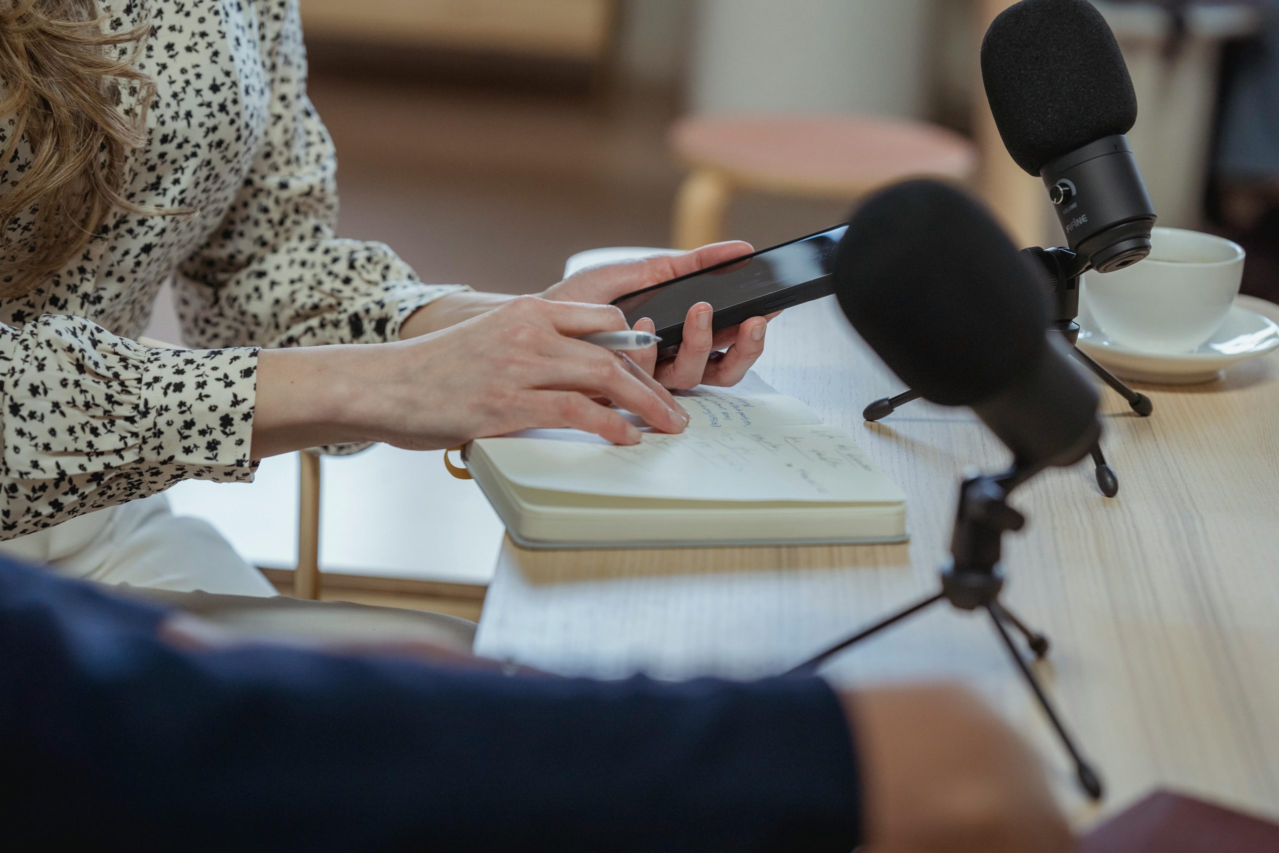 A close up view of hands holding a phone and writing notes at a table.
