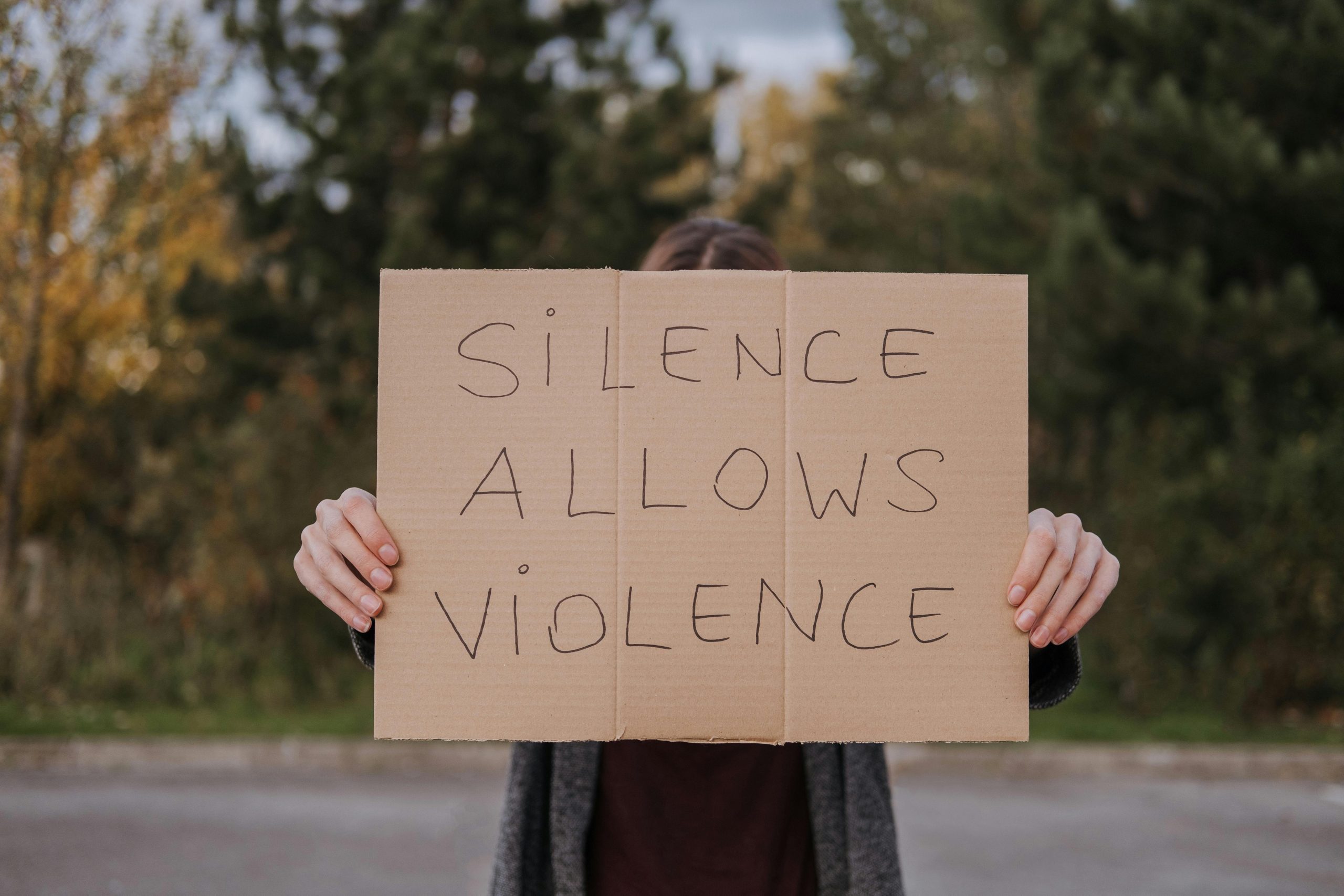 A person holding a cardboard sign that reads "Silence allows violence"