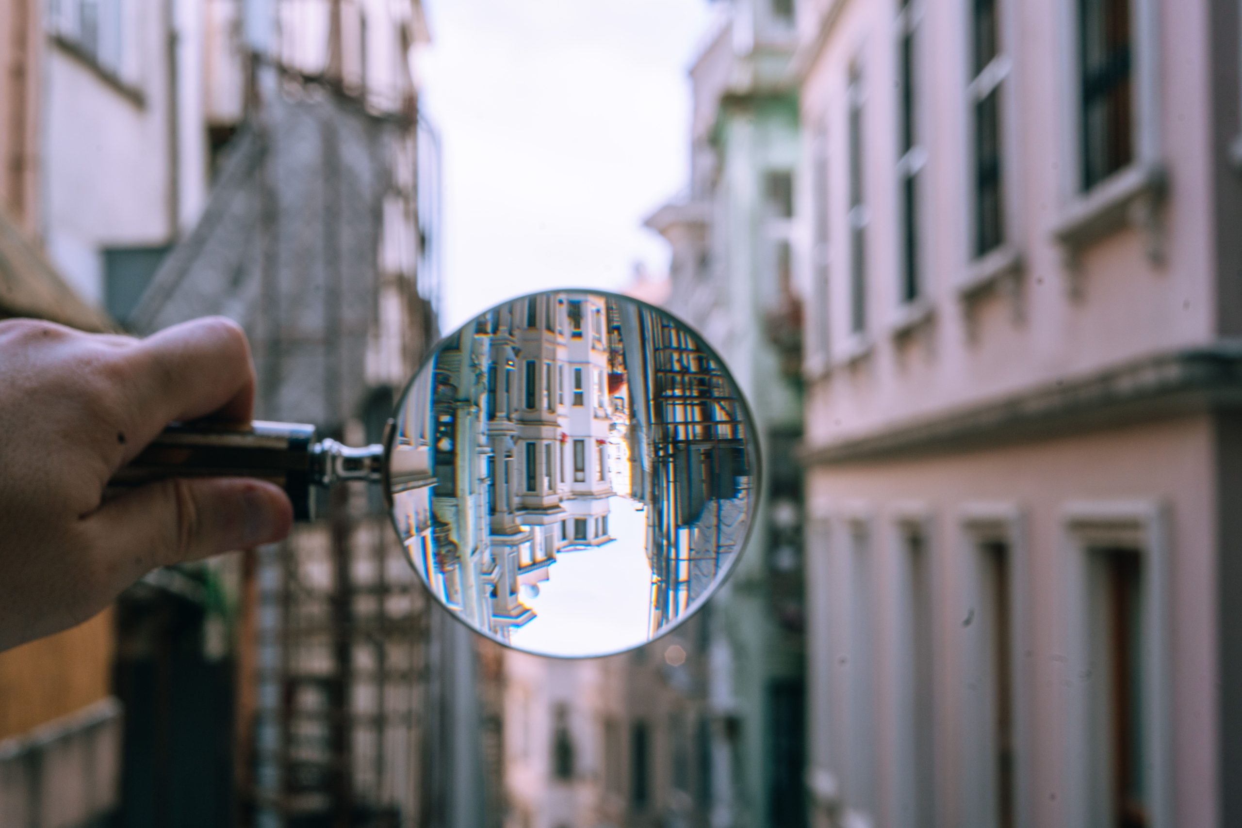 A blurry view of a city street. A hand holding a magnifying glass shows a clearer view of the buildings.